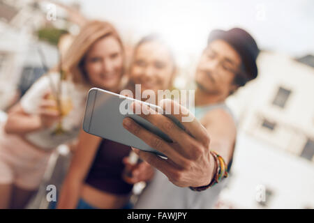 Young friends in a party taking self portrait with their smart phone. Focus on mobile phone in man's hand. Stock Photo