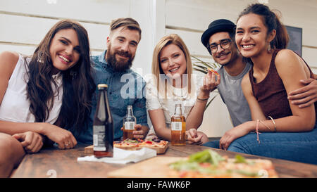 Group portrait of young friends gathered around the table at a rooftop party. Multiracial young people looking at camera and smi Stock Photo
