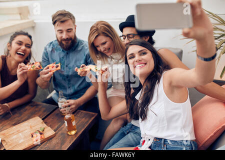 Group of friends taking selfie on a smart phone. Young people eating pizza on rooftop party taking selfie. Stock Photo