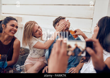 Young friends having fun at party being photographed with mobile phone. Young people sitting together enjoying party with one wo Stock Photo