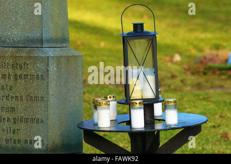 Ronneby, Sweden - December 29, 2015: Small iron table with lanterns on top. Beside is part of memorial tombstone for unnamed per Stock Photo