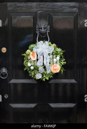 Christmas decorative wreath hung on lion door knocker on black door Stock Photo