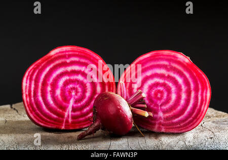 Close up of a cut red and white striped beet with an uncut small beet on top of a wooden board and black background; Calgary, Alberta, Canada Stock Photo