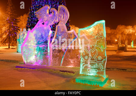 Ice sculpture in the city park on Christmas and New Year with cave paintings of deer, mythical creatures, solar signs, petroglyphs. Illuminated at night. Stock Photo