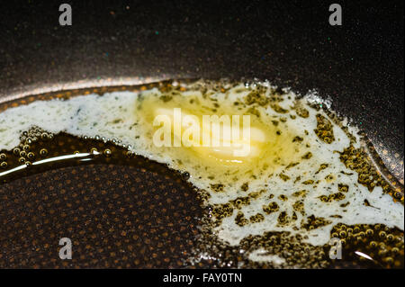 Macro close-up of piece of butter slowly melting and bubbling in black Teflon frying pan. Stock Photo