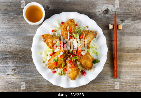 Top view of fried Asian style chicken wings in white plate with garnishes. Green tea and chopsticks in holder. Rustic wooden boa Stock Photo