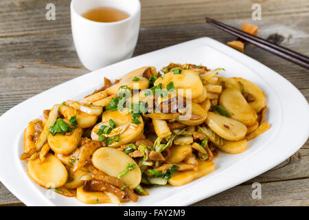 Close up front view of stir fry consisting of sliced sticky rice, onion, mushroom, and chicken. Chopsticks and tea in background Stock Photo
