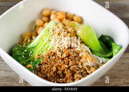Close up front view of crispy spicy chicken with noodles and bok choy in white bowl. Selective focus in middle of dish. Stock Photo