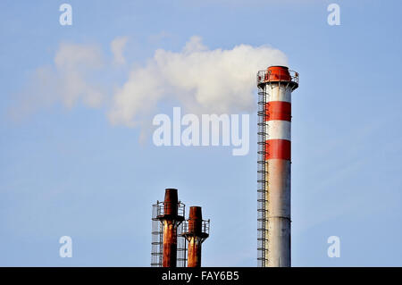 Smoke and steam coming out from an industrial petrochemical plant chimney with a blue sky on the background Stock Photo