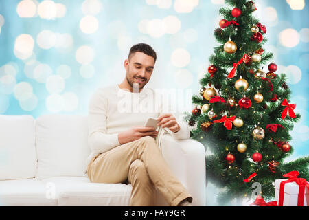 smiling man with smartphone over christmas lights Stock Photo