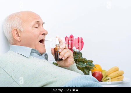 Weary senior gentleman uses his sore throat spray. Stock Photo