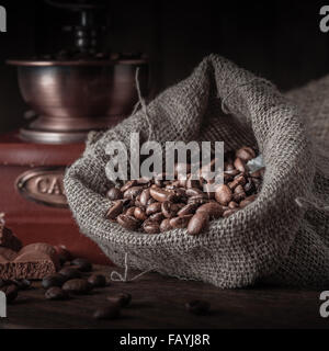 Bag of coffee beans on a dark background. Vintage coffee grinder and chocolate pieces on a wooden table. Stock Photo