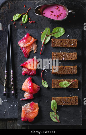 Sliced salmon filet, salted with beetroot juice, served with whole wheat toasts, salad leaves, beetroot sauce and pink pepper ov Stock Photo