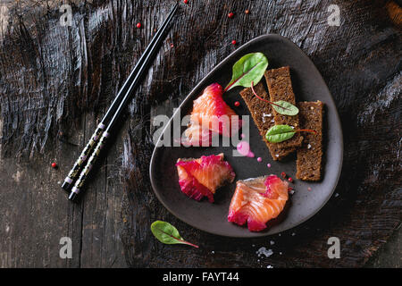 Triangular ceramic plate with Sliced salmon filet, salted with beetroot juice, served with whole wheat toasts, salad leaves and Stock Photo