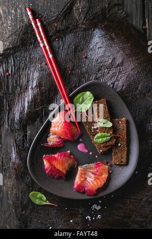 Triangular ceramic plate with Sliced salmon filet, salted with beetroot juice, served with whole wheat toasts, salad leaves and Stock Photo