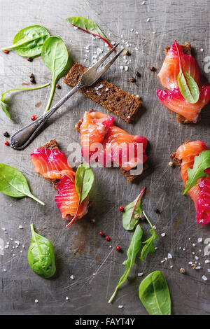 Sliced salmon filet, salted with beetroot juice, served on whole wheat toasts with salad leaves, sea salt and pepper and vintage Stock Photo