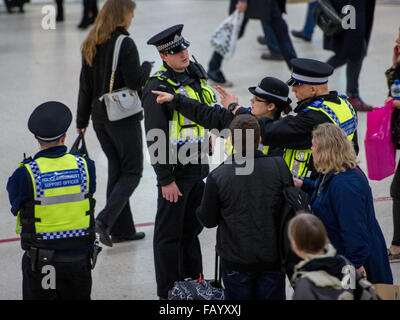 A CCTV camera watches from above as officers guard Victoria Station. The Metropolitan Police are posting more officers in Underground Stations following the suspected terrorist attack at Leytonstone Underground Station.  Featuring: Community Support Offic Stock Photo