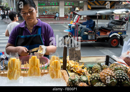 Bangkok fruit and vegetable stall holder surrounded by her produce. A street vendor gets some ice on his fresh pineapple stall in Bangkok Thailand Stock Photo