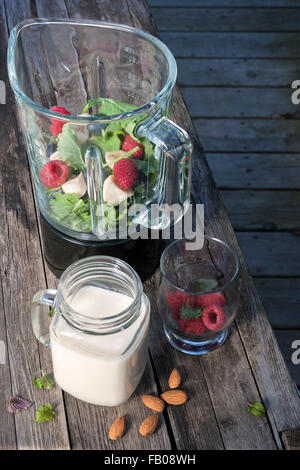 Blender with healthy smoothie ingredients - almond milk, fresh fruit, baby kale - on rustic wood table. Stock Photo