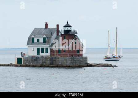 Sailboat passes by Rockland Breakwater lighthouse on a summer cloudy day in mid coast Maine during high tide. The region is famous for sailing tours. Stock Photo