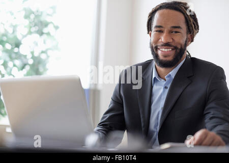 Smiley businessman sitting at desk with laptop Stock Photo