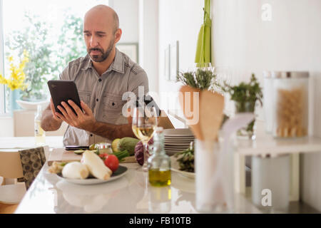 Man using digital tablet leaning on kitchen counter Stock Photo
