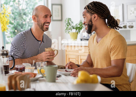 Smiley homosexual couple having breakfast in kitchen Stock Photo