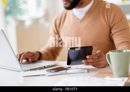 Man working with laptop at table and holding digital tablet Stock Photo