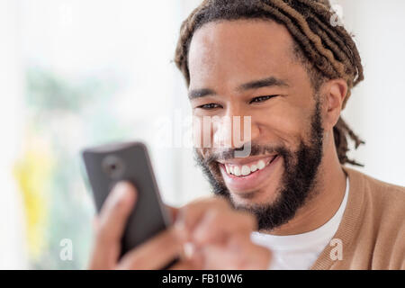 Smiley young man with dreadlocks using smart phone Stock Photo
