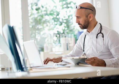 Concentrated doctor working with laptop at desk in office Stock Photo