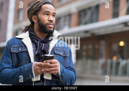 Serious man with dreadlocks holding smart phone in street Stock Photo