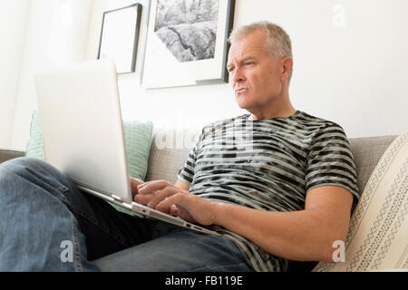 Man sitting on sofa using laptop Stock Photo