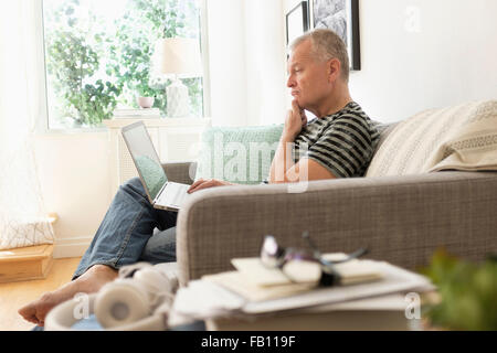 Man sitting on sofa using laptop Stock Photo
