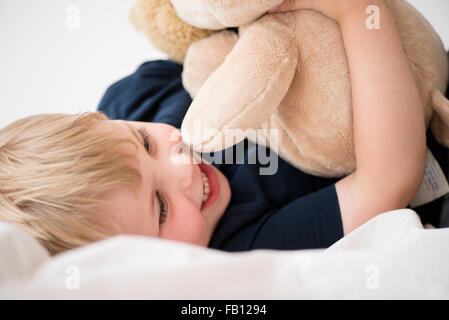 Smiling boy (2-3) with toy lying down on bed Stock Photo