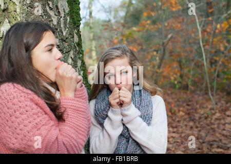 Teenage girls in forest hands over mouth mimicking animal noise, looking away Stock Photo