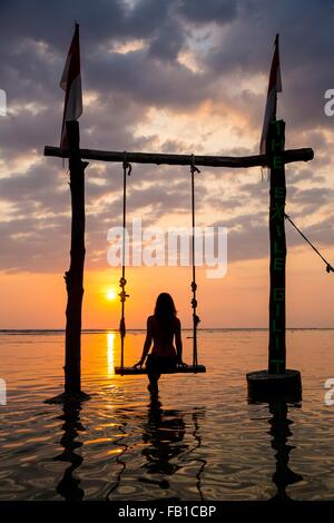 Silhouetted female tourist on swing watching sunset over sea, Gili Trawangan, Lombok, Indonesia Stock Photo