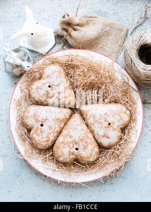 Overhead view of heart shaped gingerbread biscuits on straw covered plate Stock Photo