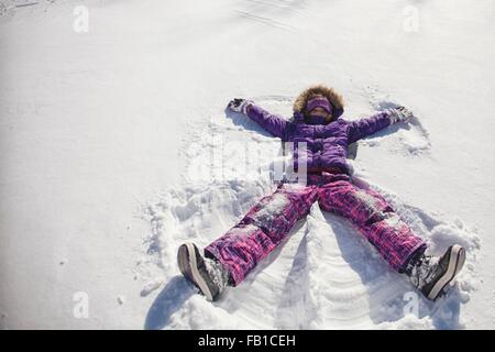 High angle view of girl wearing ski suit lying snow making snow angel Stock Photo