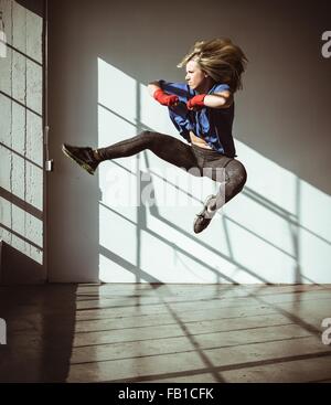 Full length view of young woman in gym in mid air in kickboxing stance Stock Photo