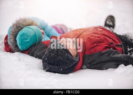 Father and daughter wearing knit hats lying on backs in snow Stock Photo