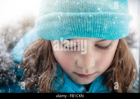 Close up portrait of girl wearing knit hat looking down, snowing Stock Photo