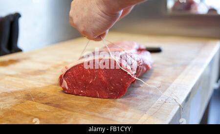 Close up of butchers hands tying meat joint in butchers shop Stock Photo