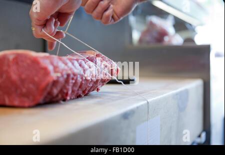 Close up of butchers hands tying meat joint on butchers block Stock Photo