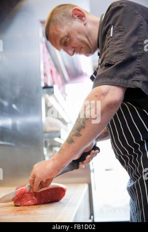 Mature butcher slicing raw steaks in butchers shop Stock Photo