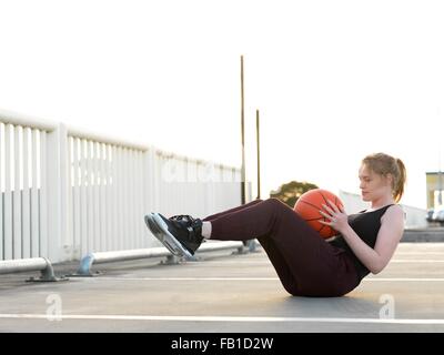 Young female basketball player doing sit-ups in parking lot Stock Photo