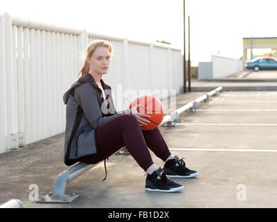 Young female basketball player sitting in parking lot