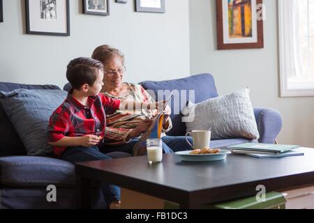 Boy pointing at book whilst reading with grandmother on sofa Stock Photo