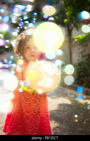 Girl wearing dress using bubble gun blowing bubbles Stock Photo