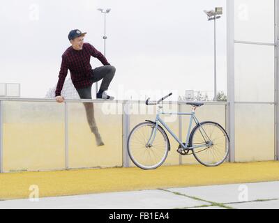 Urban cyclist climbing over fence on sports field Stock Photo