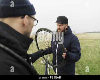 Urban cyclists fixing tyre in field Stock Photo
